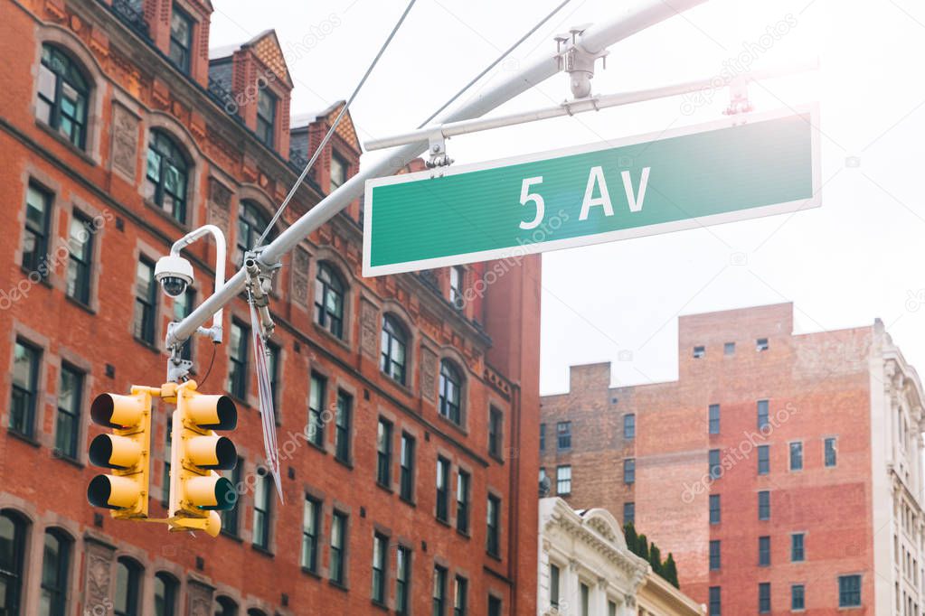 Fifth avenue sign in Manhattan New York. Traffic light at intersection with the famous 5th fifth avenue in New York city with red brick buildings on background. Travel and transportation concepts.