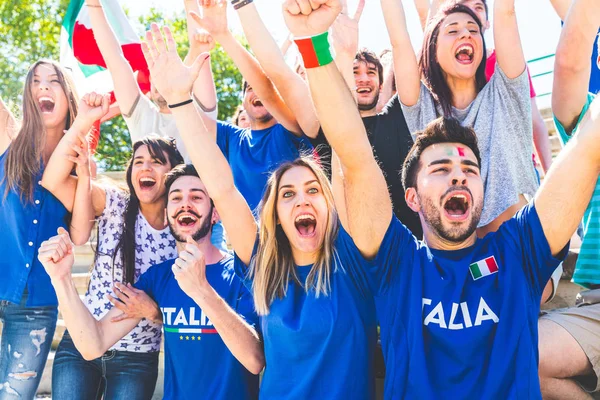 Italian supporters celebrating at stadium with flags. Group of fans watching a match and cheering team Italy. Sport and lifestyle concepts.