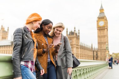Cep telefonu ile Big Ben arka plan üzerinde seyir kız Londra'da çok ırklı grup. Londra'daki üç kadınlar birlikte eğleniyor. Seyahat ve dostluk kavramları