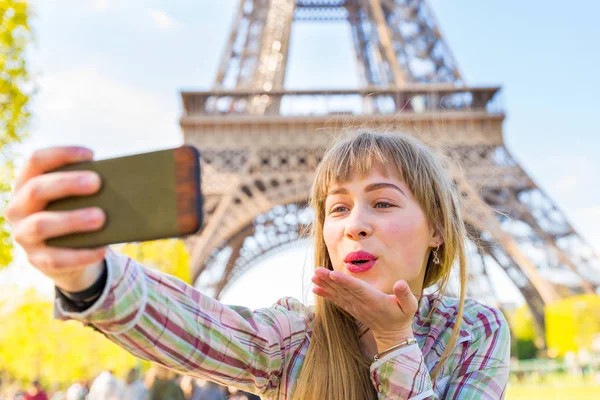 Kız bir selfie alarak ve arka plan üzerinde Eyfel Kulesi ile Paris'te bir öpücük üfleme. Video aramasý ile onun smartphone üzerinde mutlu sarışın genç kadın. Seyahat, teknoloji ve yaşam tarzı kavramları