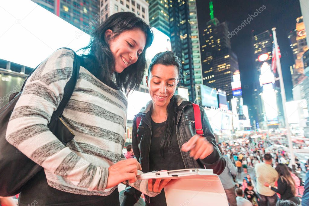 Girls in New York looking at a smart phone or digital tablet. Beautiful young women, tourists in New York city, having fun at night in the city that never sleeps