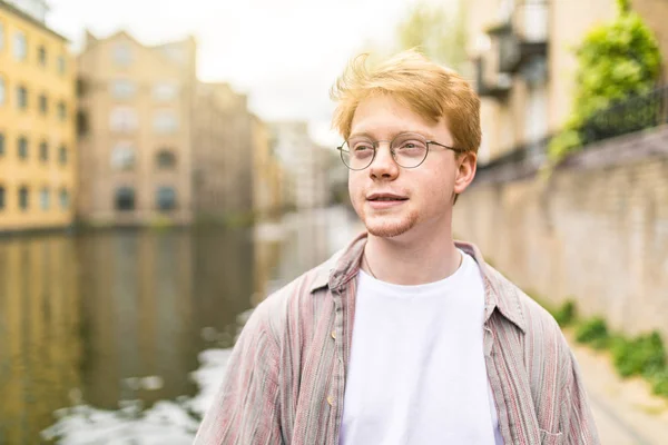 運河沿いでの生姜髪男の肖像画 若くて丸眼鏡 ロンドンのカメラから見て薄いシャツを着て 赤い髪を持つ男 — ストック写真