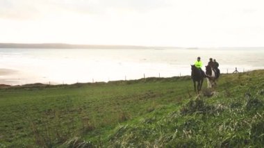 Kırsal kesimde ata binerek insanlar. Üç kişi ve okyanus ve arka plan uçurumlarda at üzerinde yeşil alanları ile. Spor, boş zaman ve seyahat kavramları