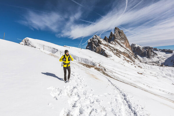 Man hiking on top of snowy mountain. Happy hiker wearing a yellow jacket walking on the snow at altitude with beautiful view on background. Adventure and travel concepts