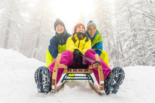 Friends having fun on the snow sliding with a little sled. Girl being pushed by two boys on a sledge. Winter sport and lifestyle,