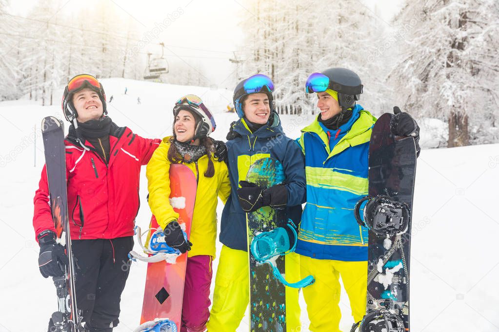 Group of friends on the snow with ski and snowboard on the slopes after skiing. Mountain ski resort with ski lift on background and people, a group of best friends, having fun in winter with snow.