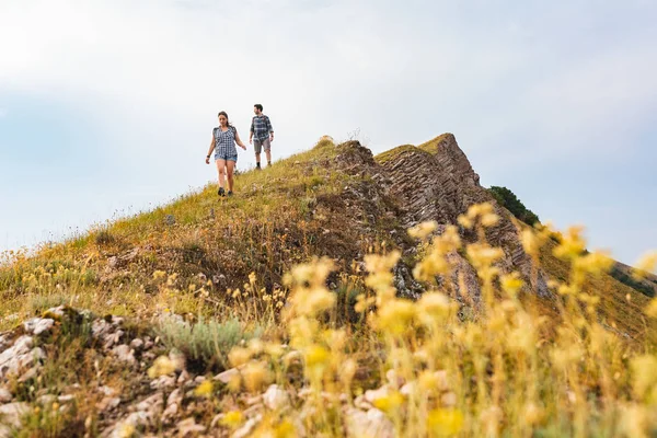 Couple walking and hiking at mountains in spring. Outdoor leisure activity on top of a mountain. Flower on foreground and people on background.