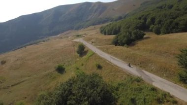Bir adam bir motosiklet sürüş bir dağ yolda hava görünümünü. Motosiklet kırsal virajlı bir yolda dron video. Ulaşım ve seyahat kavramları