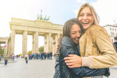 Mutlu kızlar Berlin'de buluşuyor ve kucaklıyorlar. İki genç kadın arka planda Brandenburg Gate ile mutluluk ve sevgi paylaşımı. Mutluluk, yaşam tarzı ve turizm kavramları