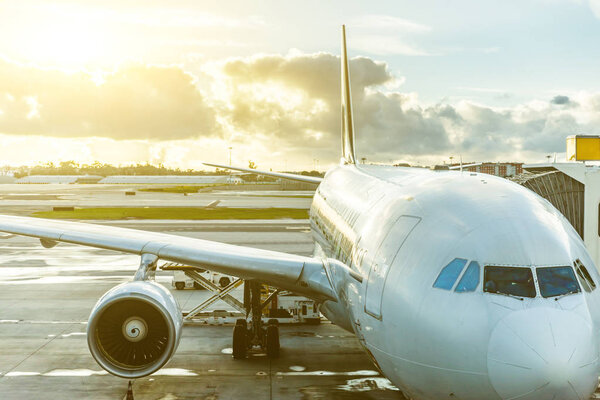 Airplane at airport close up view at sunset. Long haul flight big aircraft ready to leave from gate. Dramatic sky with clouds at sunset. Travel and transportation concepts