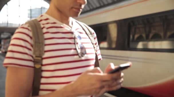 Man at train station checking timetables on mobile phone — Stock Video