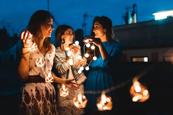 Mulheres felizes se divertindo na festa no telhado com luzes à noite — Fotografia de Stock