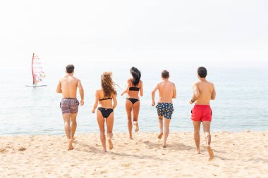 Barcelona 'da kumsalda eğlenen arkadaşlar, yaz tatilinde birlikte yüzmek için koşan çok ırklı arkadaşlar, İspanya' da seyahat ederken mutluluk ve dostluk.