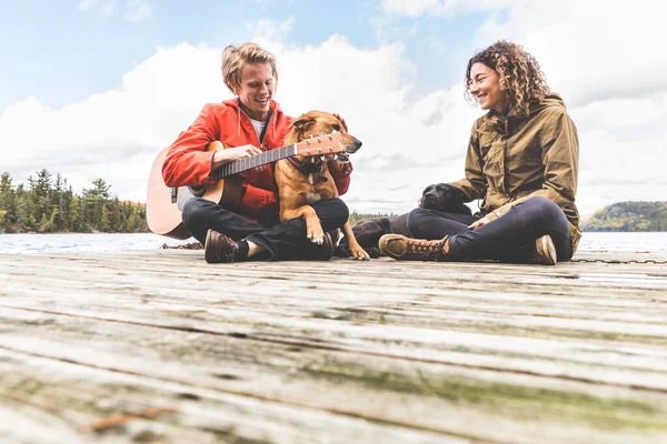 一对快乐的年轻夫妇在码头上玩着他们的狗和吉他 秋天在加拿大的一个湖边 男人和女人恋爱了 大自然的爱情和生活方式 — 图库照片
