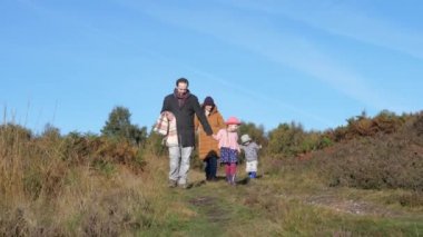 Mutlu bir aile, güneşli bir sonbahar gününde kırsalda birlikte yürüyor. İki çocuklu ebeveynler, İngiltere 'de ormanda eğleniyor. Doğa ve yaşam tarzı kavramları.