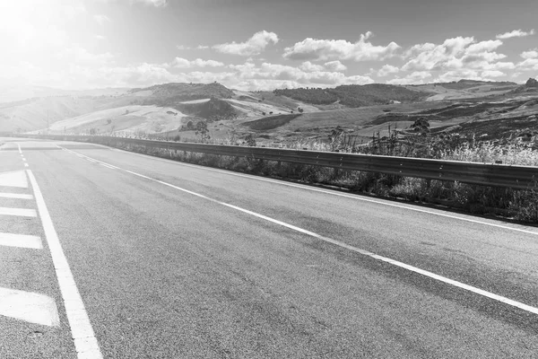 Gündoğumunda Sicilya tepelerinin manzarası. Asfalt yolu Sicilya adasının sık sık depremlerinden dolayı sütunlarla yükseldi. Siyah beyaz resim