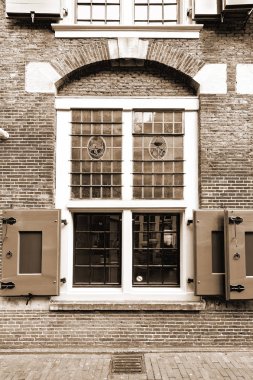Stained glass window of the traditional house in Amsterdam. Red brick facade of the old city house in Holland. Vintage Style Sepia photo clipart