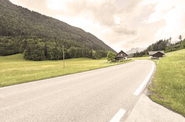 Ormanlar, alanları, otlaklar ve çayırlar karla kaplı Alps arka plan üzerinde Avusturya peyzaj asfalt yol. Vintage tarzı 
