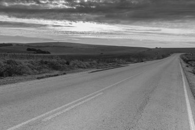 Tepeler arasındaki asfalt yol alanları İspanya güneş doğarken kaplı. Yasaklayıcı trafik işaret yok bir yolda sollama. Siyah ve beyaz fotoğraf.