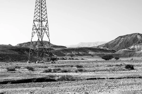 Electrical power lines on pylons in the landscape of the Middle East. Rocky hills of the Negev Desert in Israel. Breathtaking landscape of the rock formations.  Black and white photography