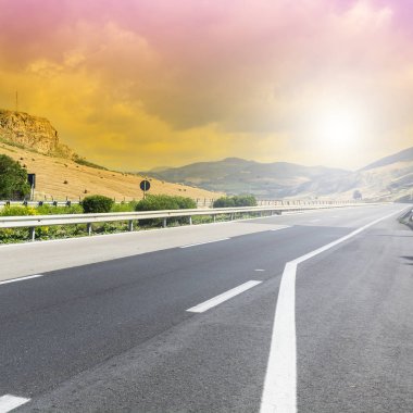 Gündoğumunda Sicilya tepelerinin manzarası. Asfalt yolu Sicilya adasındaki sık depremler nedeniyle sütunlarla yükseltildi.