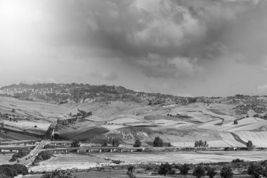 Gündoğumunda Sicilya tepelerinin manzarası. Asfalt yolu Sicilya adasının sık sık depremlerinden dolayı sütunlarla yükseldi. Siyah beyaz resim