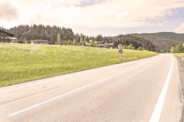 Asphalt road in Austrian landscape with forests, fields, pastures and meadows. Vintage style
