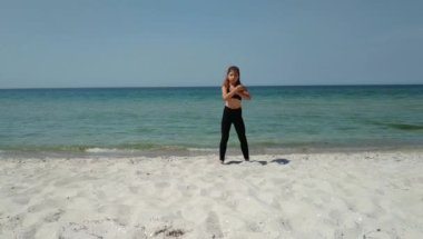 koyu spor giyim küçük kız deniz tarafından kum üzerinde karate kata eğitim yapan