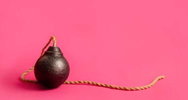 Klasik yuvarlak siyah antika bomba. Pembe arka planda uzun, yanmayan bir ip fitili var.