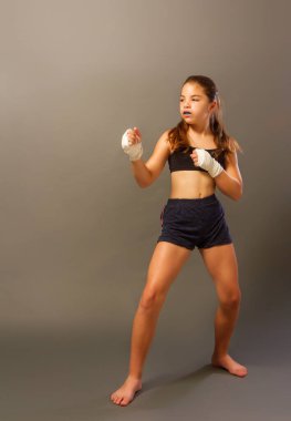 Kolsuz tişörtlü ve elleri bandaja sarılı küçük bir kız karanlık bir arka planda dövüş sanatlarıyla meşgul.