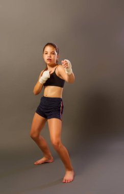 Kolsuz tişörtlü ve elleri bandaja sarılı küçük bir kız karanlık bir arka planda dövüş sanatlarıyla meşgul.