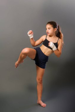 Kolsuz tişörtlü ve elleri bandaja sarılı küçük bir kız karanlık bir arka planda dövüş sanatlarıyla meşgul.