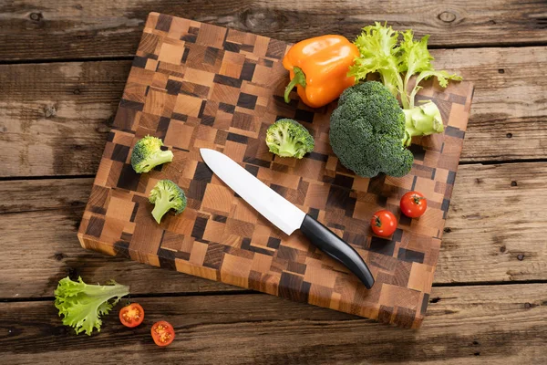 Яскраві помідори і перець лежать на дерев'яній обробній дошці біля кухонного ножа . — стокове фото
