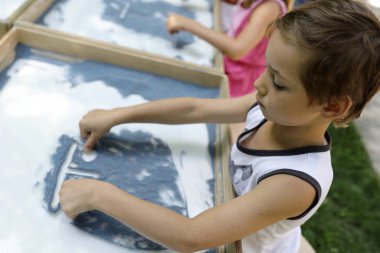 Çocuk kum üzerinde beyaz masa ile boyar