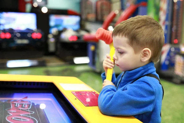 Boy playing arcade game with hammer in amusement center