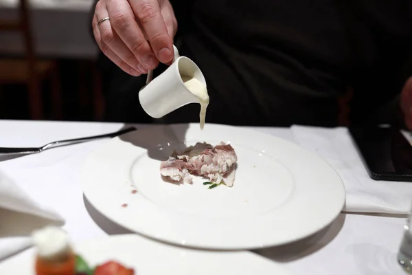 Person pouring sauce on whitefish in restaurant