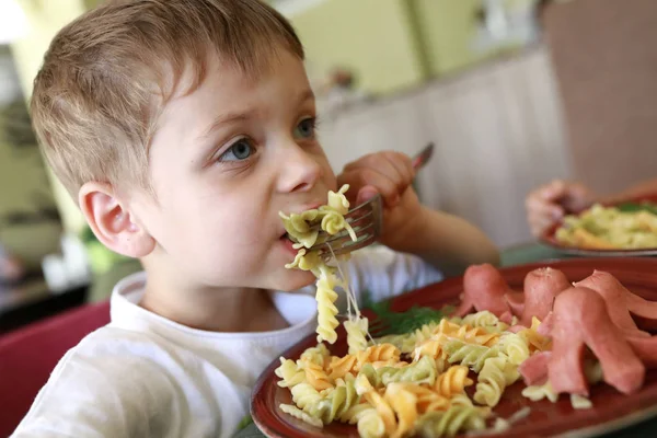 O miúdo tem massa com salsichas. — Fotografia de Stock