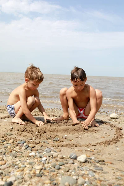 Kardeşler sahilde çakıl taşları ile oynuyor — Stok fotoğraf