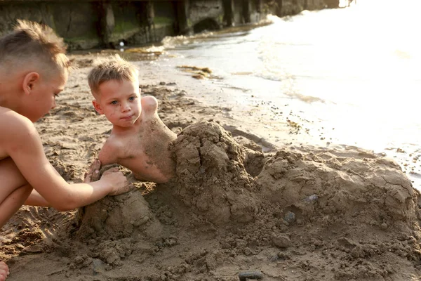 Boy burying his brother in sand — Stock Photo, Image