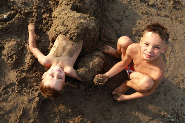 Child buries his brother in sand — Stock Photo, Image