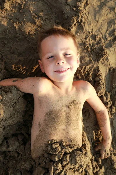 Happy kid buried in sand on beach — Stock Photo, Image