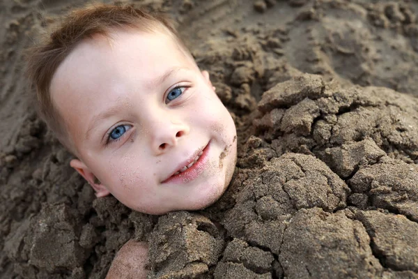 Garçon souriant enterré dans le sable sur la plage — Photo