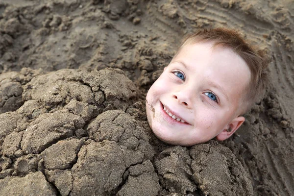 Enfant souriant enterré dans le sable sur la plage — Photo