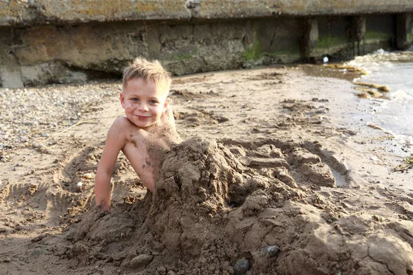 Preschooler buried in sand on beach — Stock Photo, Image