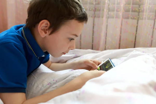 Child playing in smartphone on bed at home