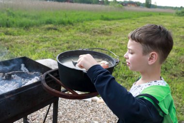 Çocuk kazanda ateşte pişirilen balık çorbasının tadını aldı.