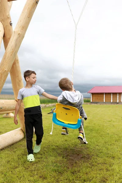Junge Schwingt Bruder Auf Schaukel Auf Spielplatz — Stockfoto