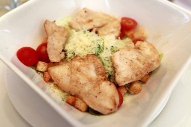Restoranda beyaz tabakta tavuk göğsü ve Sezar salatası.