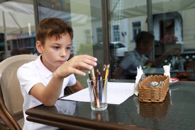 Restoranın terasında kalemle çizim yapan çocuk.