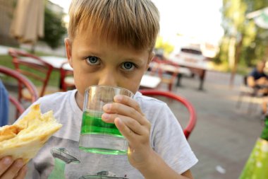Çocuk açık hava restoranında yeşil limonata içiyor.